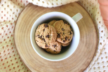Mug filled with chocolate chip cookies and soft knitted blanket on a bed. Flat lay.