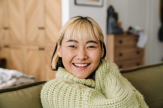 Asian teen girl with piercing smiling while resting on sofa