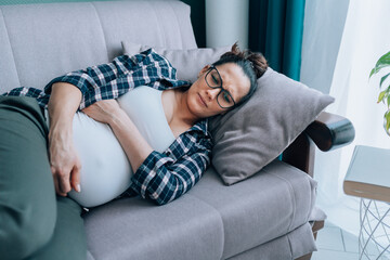 Depression in pregnancy. Young sad lonely pregnant woman lying on sofa at home, having depressed...