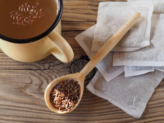 Herbal tea drink, linseed in wooden spoons, tea filter bags on wooden background, top view, flat layout. Useful linum plant with omega and vitamins for use in medicine and vegetarian dietary nutrition