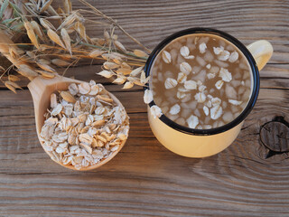Natural useful oatmeal drink in a mug, oat flakes in a spoon and spikelets of Avena sativa grain grass on a wooden background. Healthy food made from oats for vegan and vegetarian food