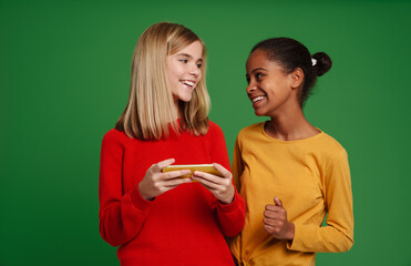 Multiracial two girls smiling together while using cellphone