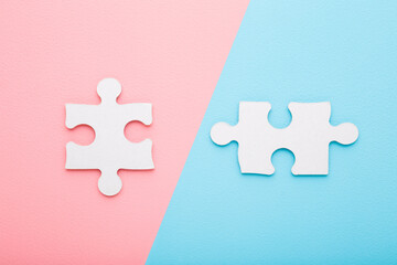 Two white puzzle pieces on light pink blue table background. Pastel color. Closeup. Concept of...