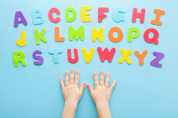Toddler boy hands with colorful letters on light blue table background. Pastel color. Time to...