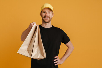 White delivery man in cap smiling while posing with paper bags