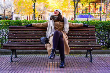 Elegant adult woman smiling and pensive, sitting on a wooden bench