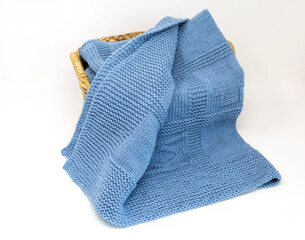 Light blue knitted blanket in geometric pattern in basket on white background