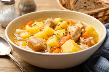Meat stew with potato and carrot in bowl on wooden background