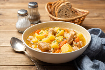 Meat stew with potato and carrot in bowl on wooden background