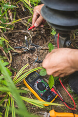 An electrician tests an exposed grounded wire with a digital multimeter with LCD screen. Safety...