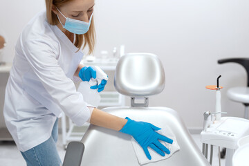 Dentist assistant wipes chair before appointment vith patient