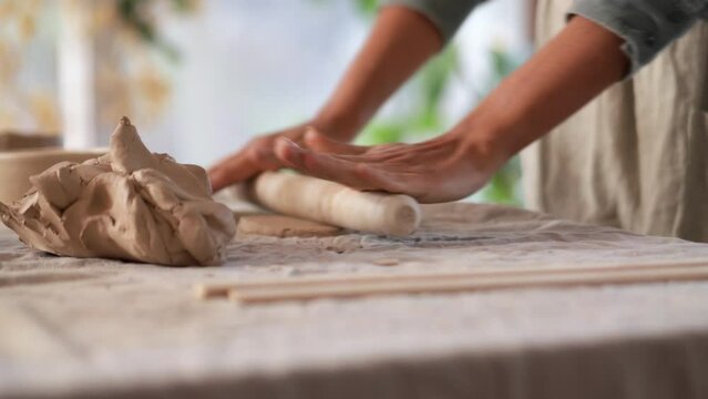 Female hands rolling out clay with a rolling pin at home