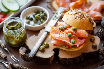 Delicious kamut bun sandwich with smoked salmon, caper spread, tomatoes and caper buds on a rustic wooded cutting board
