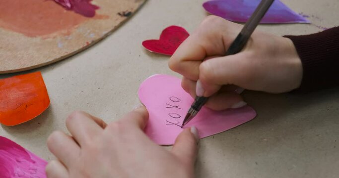 Signing handmade cards for Valentine's Day with words XO XO. Making crafted hearts, homemade gifts. Preparing for Valentine Day, close-up with unrecognizable woman