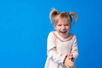 Cheerful charming little girl smiling and laughing against blue background