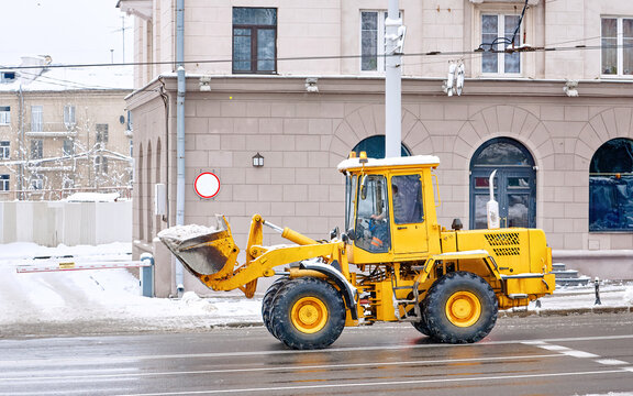 Front loader removing snow from city road and sidewalk after blizzard. Heavy duty loader removing snow with shovel blade, snowplow, snow removal works, wheel loader clearing snowy road