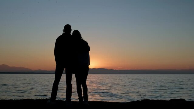 Silhouette of young couple hugging against sea and sunset