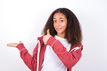 teenager girl wearing pink jacket standing against wite background Showing palm hand and doing ok gesture with thumbs up, smiling happy and cheerful.