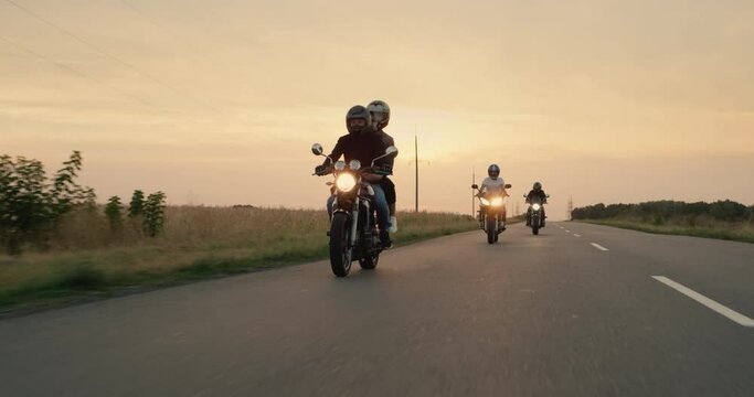 Three bikers drive on the highway at sunset