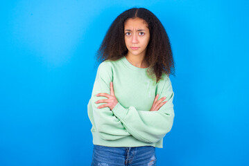Fototapeta na wymiar beautiful teenager girl wearing green sweater standing against blue background Pointing down with fingers showing advertisement, surprised face and open mouth