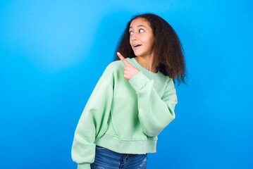 beautiful teenager girl wearing green sweater standing against blue background glad cheery demonstrating copy space look novelty