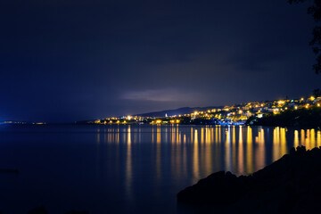 Obraz premium The lights of Novi Vinodolski town are reflected in the coastal waters of Adriatic sea in Croatia