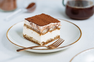 Tiramisu cake dessert served with coffee, biscuit and cocoa as ingredients on a bright white background. One piece of cake