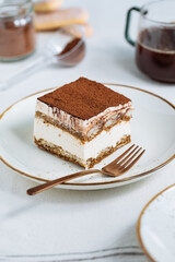 Tiramisu cake dessert served with coffee, biscuit and cocoa as ingredients on a bright white background. One piece of cake