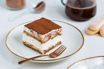 Tiramisu cake dessert served with coffee, biscuit and cocoa as ingredients on a bright white background. One piece of cake