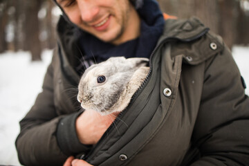 Close portrait of a man with a rabbit. The boy gently hugs a gray fluffy rabbit, a happy childhood