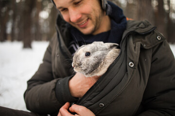Close portrait of a man with a rabbit. The boy gently hugs a gray fluffy rabbit, a happy childhood