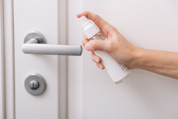 Cleaning white door handles with an antiseptic wet wipe and sanitizer spray. Disinfection in hospital and public spaces against corona virus. Woman hand using towel for cleaning home room door link