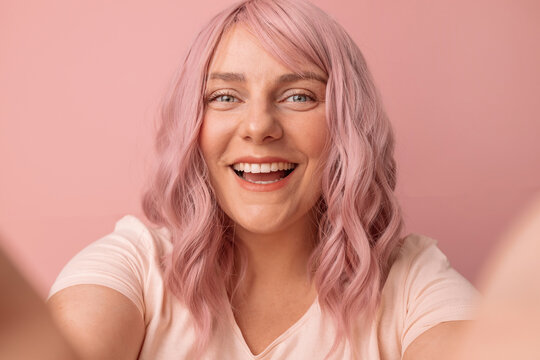 Cropped shot of happy woman looking at camera and smiling, making selfie on isolated pink background