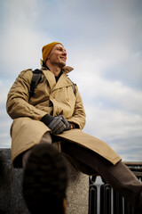 Traveler man in vintage winter coat enjoying city view in Ukraine, sitting on bridge near Dnipro rive. 