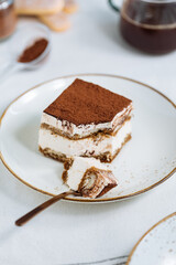 Tiramisu cake dessert served with coffee, biscuit and cocoa as ingredients on a bright white background. One piece of cake