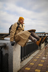 Traveler man in vintage winter coat enjoying city view in Ukraine, sitting on bridge near Dnipro rive. 