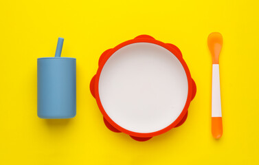 Set of plastic dishware on yellow background, flat lay. Serving baby food