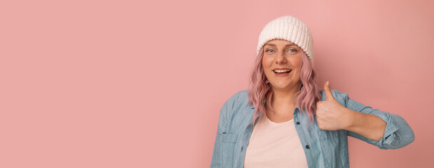 Obraz na płótnie Canvas Attention promotions banner. Charming young caucasian woman in a white knitted hat with pink hair showing thumb up like gesture isolated on pastel background, banner, panorama, copy space