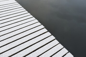 Snow-covered modern wooden pier (jetty, boardwalk) over the frozen river. Ice, frost, snow...