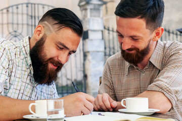 Two hipster freelance businessmen working outdoors on the project and drinking coffee. Concept: happiness, freedom and favorite job. Horizontal image.