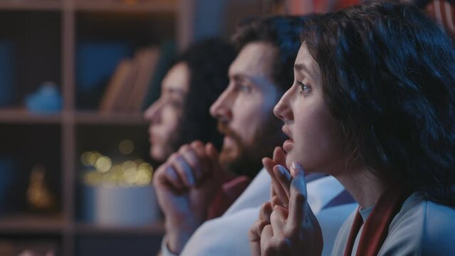 Concentrated football fans supporting favorite team while watching match on TV sitting on sofa at home. Multiracial people watching soccer game and feeling nervous while waiting for a goal.