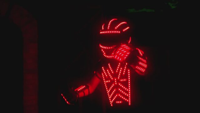 Man dressed in led illuminated costume with colorful lights dancing and moving inside dark interior or club . Dancer guy wearing clothing with neon lights on his body and dances . Shot on ARRI camera