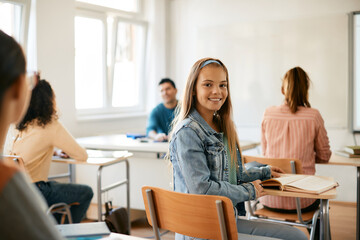 Happy teenage girl looking at camera during lecture at high school. - obrazy, fototapety, plakaty