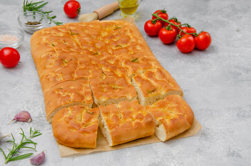 Traditional Italian Focaccia with rosemary, garlic, sea salt and olive oil on a gray concrete background.