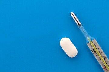 On a blue background lies a thermometer and pelvic tablets.