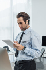 guard in earphone and shirt with security lettering using digital tablet in office.