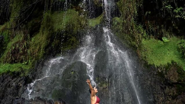 Full length view of caucasian woman in swimsuit at thermal springs in Colombia. Panoramic view from top to bottom of woman underneath a big waterfall in the jungle. Colombia travel destination