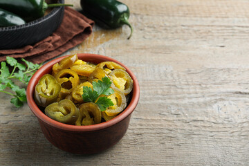 Bowl with slices of pickled green jalapeno peppers on wooden table, space for text
