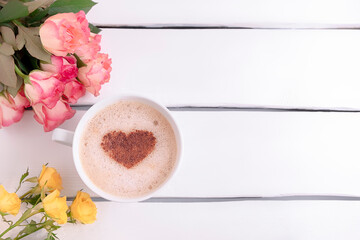 Top view of coffee mug with cinnamon heart shape and beautiful roses on white wooden table, copy space