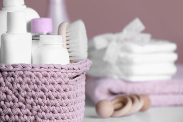 Fototapeta na wymiar Baby cosmetic products and hair brush in knitted basket on white table, closeup. Space for text
